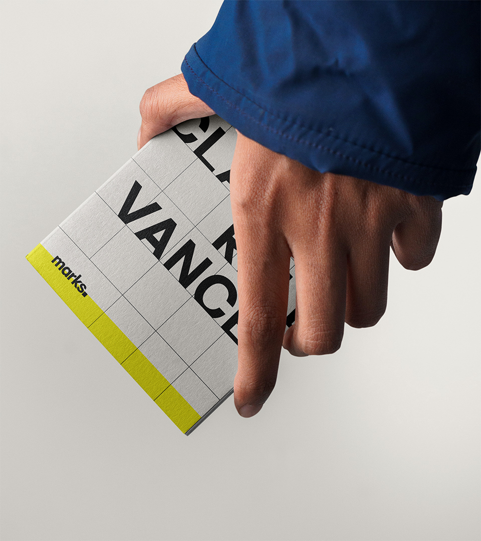 Hand wearing blue sleeve holding a gray notebook with black text and yellow accent.