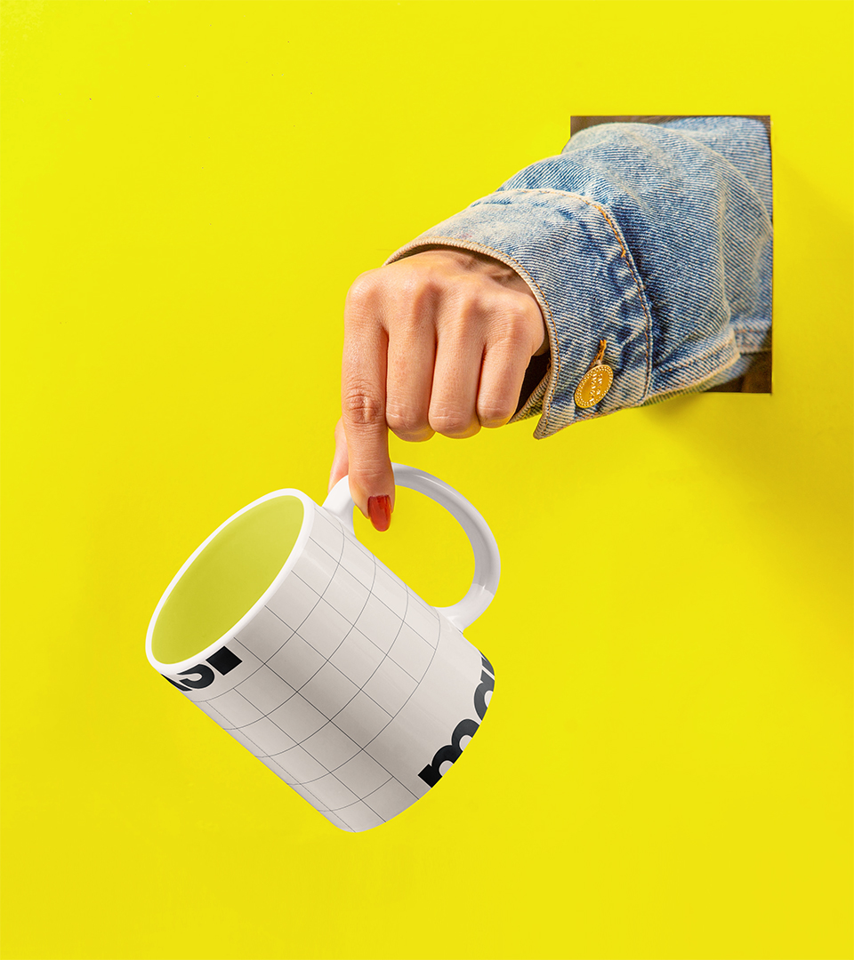Hand in denim jacket sleeve holding a white grid patterned mug against a bright yellow background.