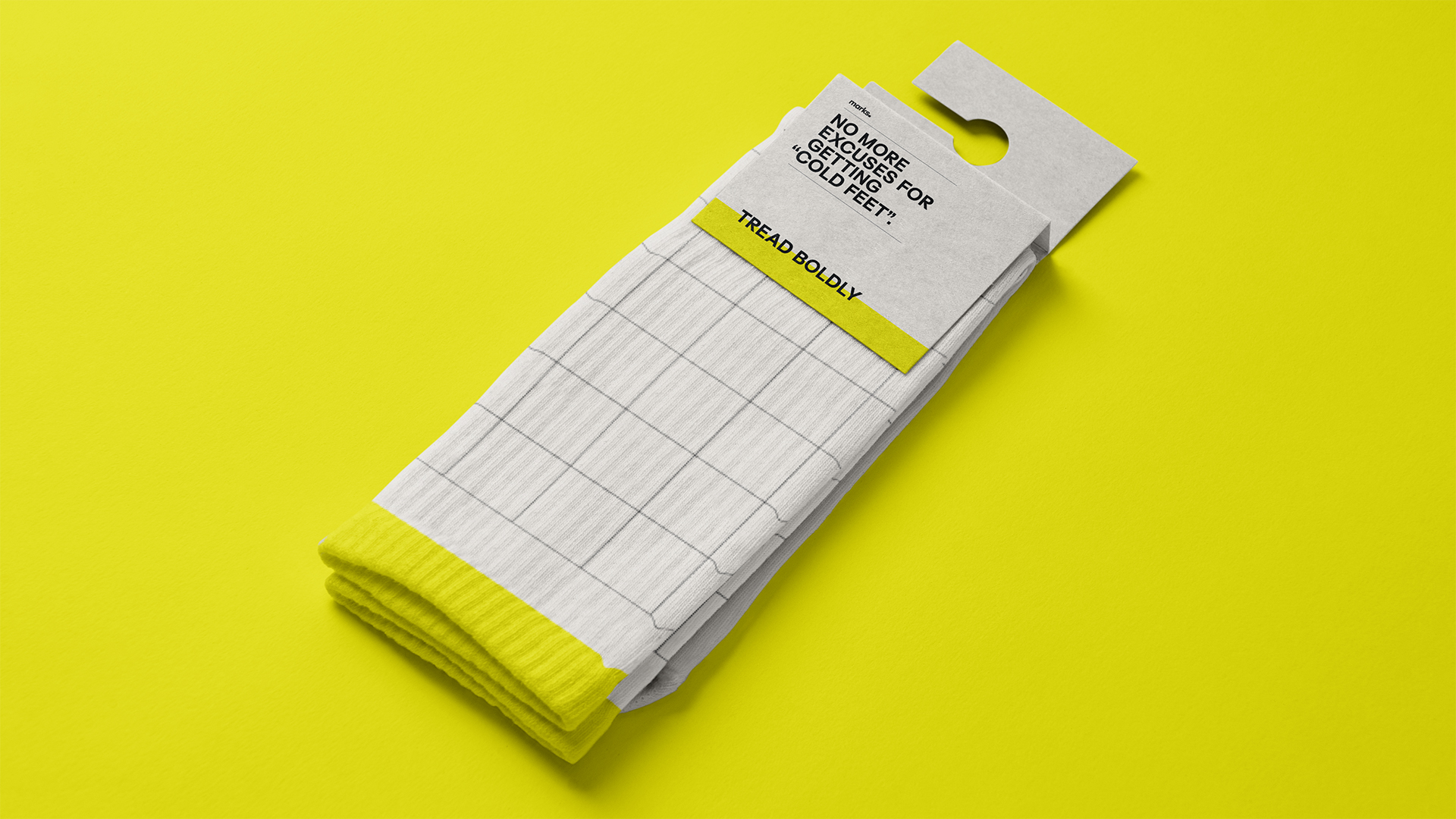 Folded white socks with a grid pattern and yellow ribbed cuffs on a yellow background, with packaging that reads 'No more excuses for getting cold feet!' and 'Tread boldly'.