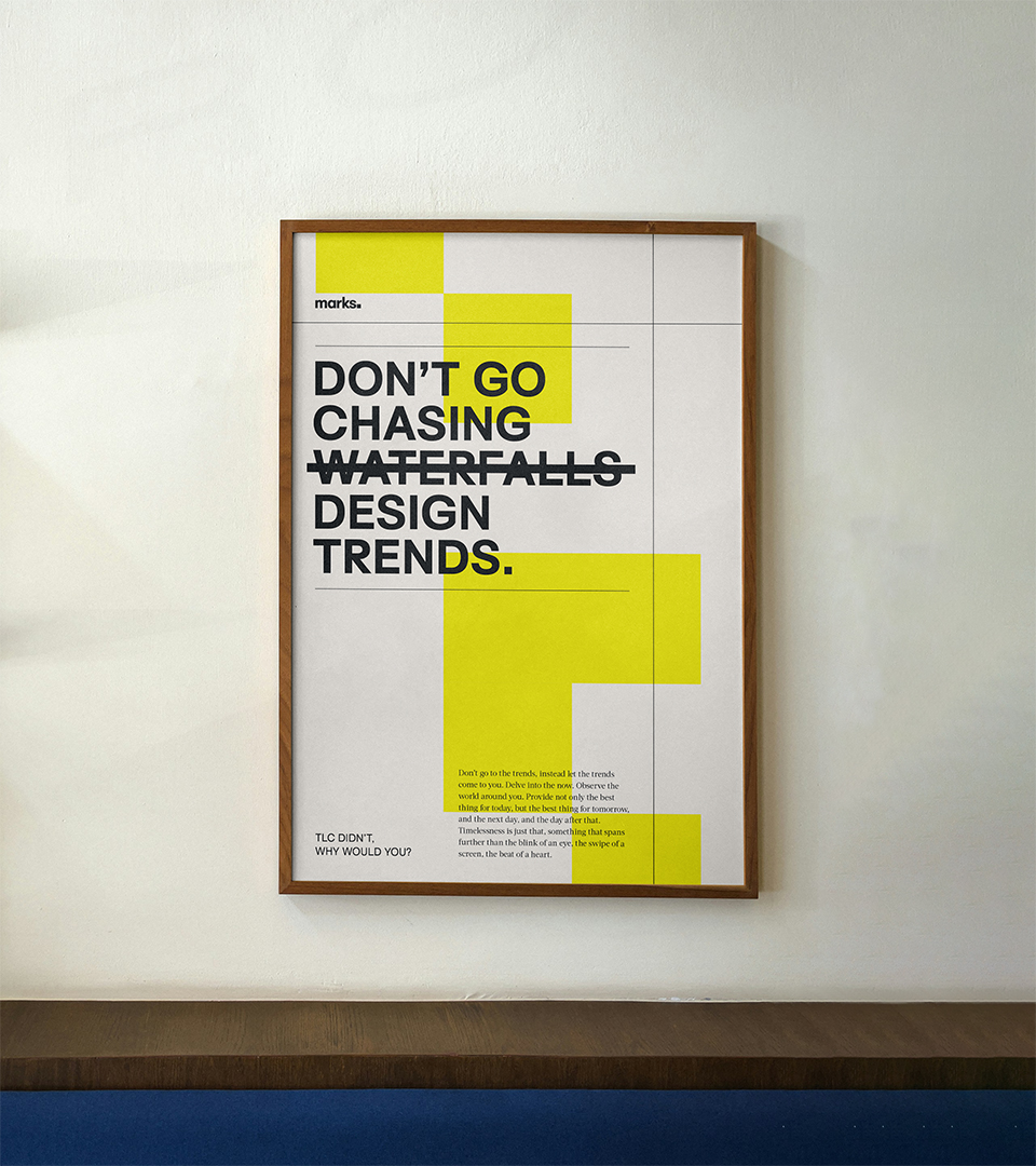 Framed poster on a white wall with the text: "DON'T GO CHASING WATERFALLS" with 'WATERFALLS' crossed out and replaced by "DESIGN TRENDS." in bold black letters, accented by yellow blocks.
