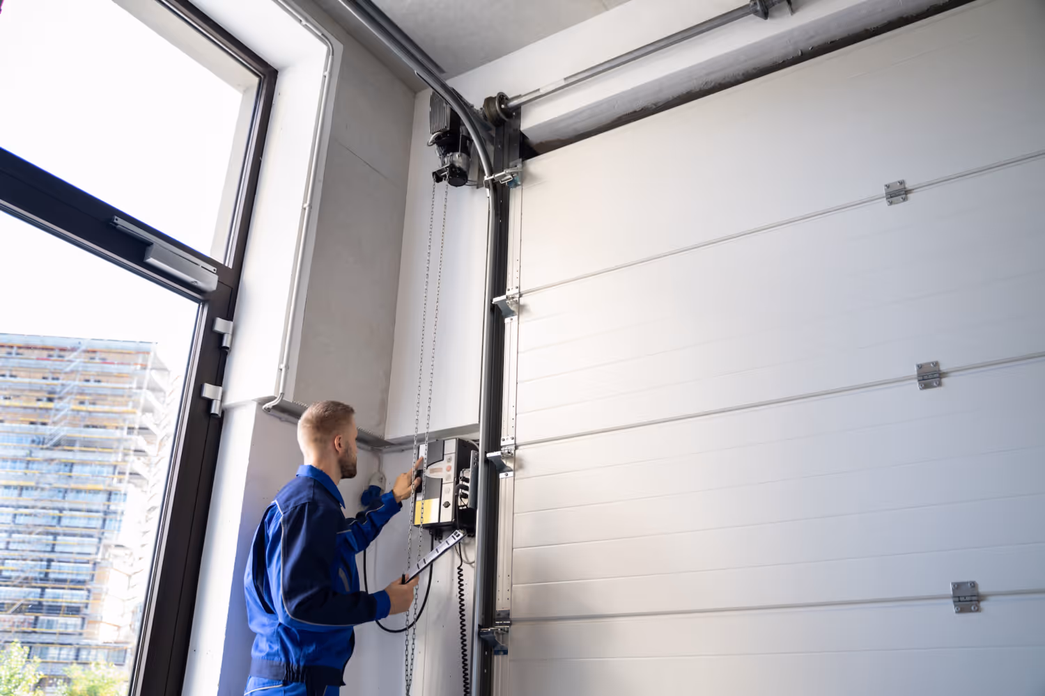 Technician in blue uniform inspecting a commercial garage door control panel inside a building.