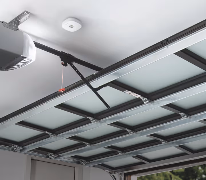 Interior view of a partially open garage door with metal framing and frosted glass panels, featuring an automatic garage door opener attached to the ceiling.