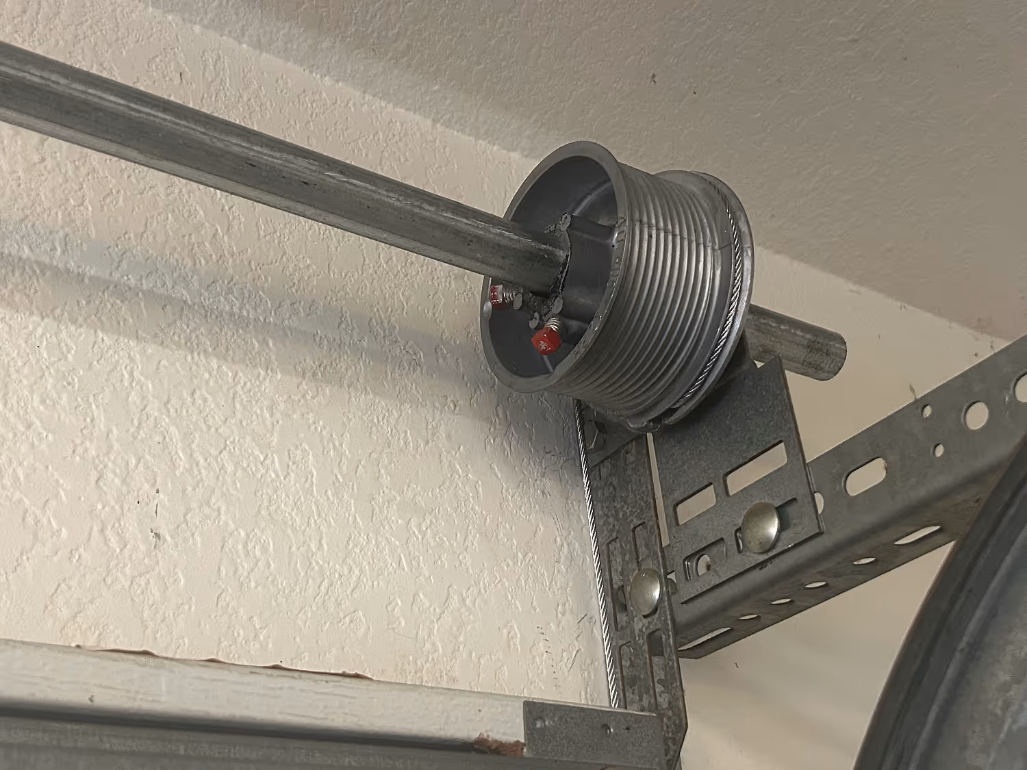 Close-up of a metal garage door torsion spring assembly mounted on a textured wall.