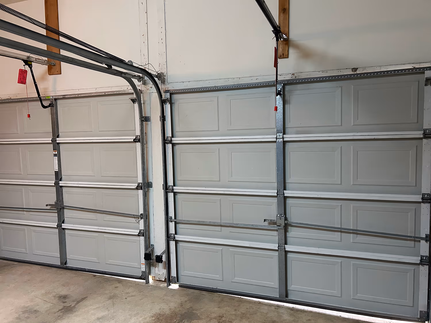 Interior view of a garage with two closed gray sectional garage doors and concrete flooring.
