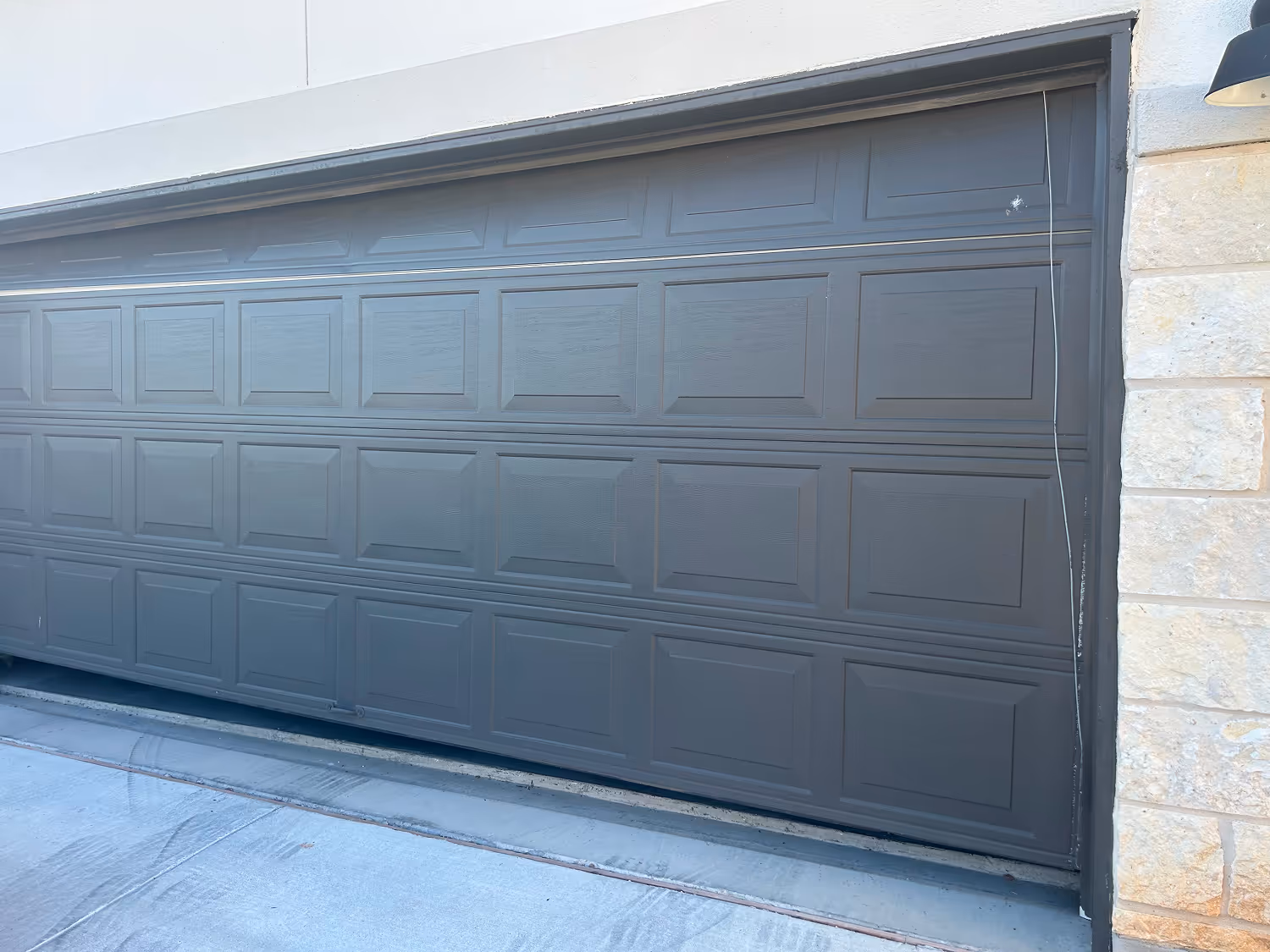 Closed dark gray sectional garage door with stone wall on the right and concrete driveway in front.