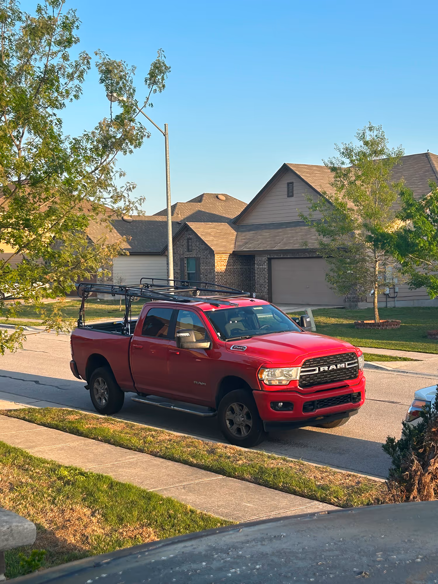 Red RAM pickup truck parked on a residential street in front of houses with trees and a clear blue sky.