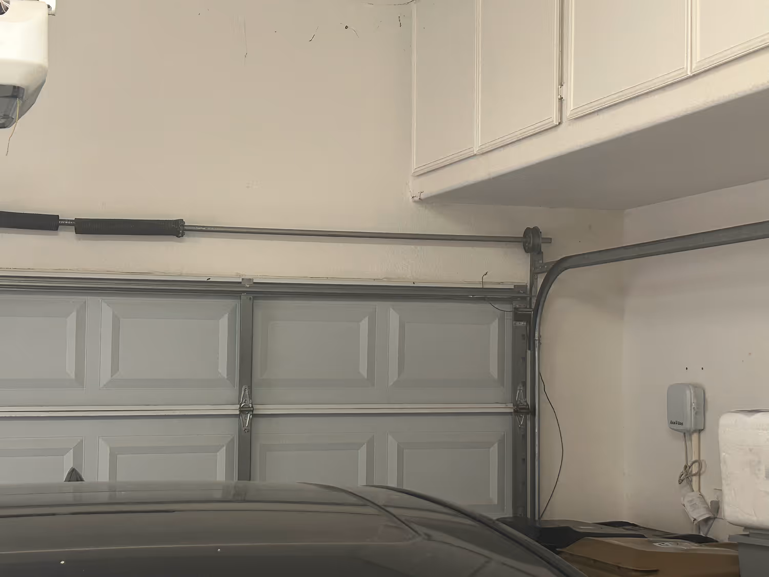 Partially visible car inside a garage with a closed light gray sectional garage door and white cabinets above.