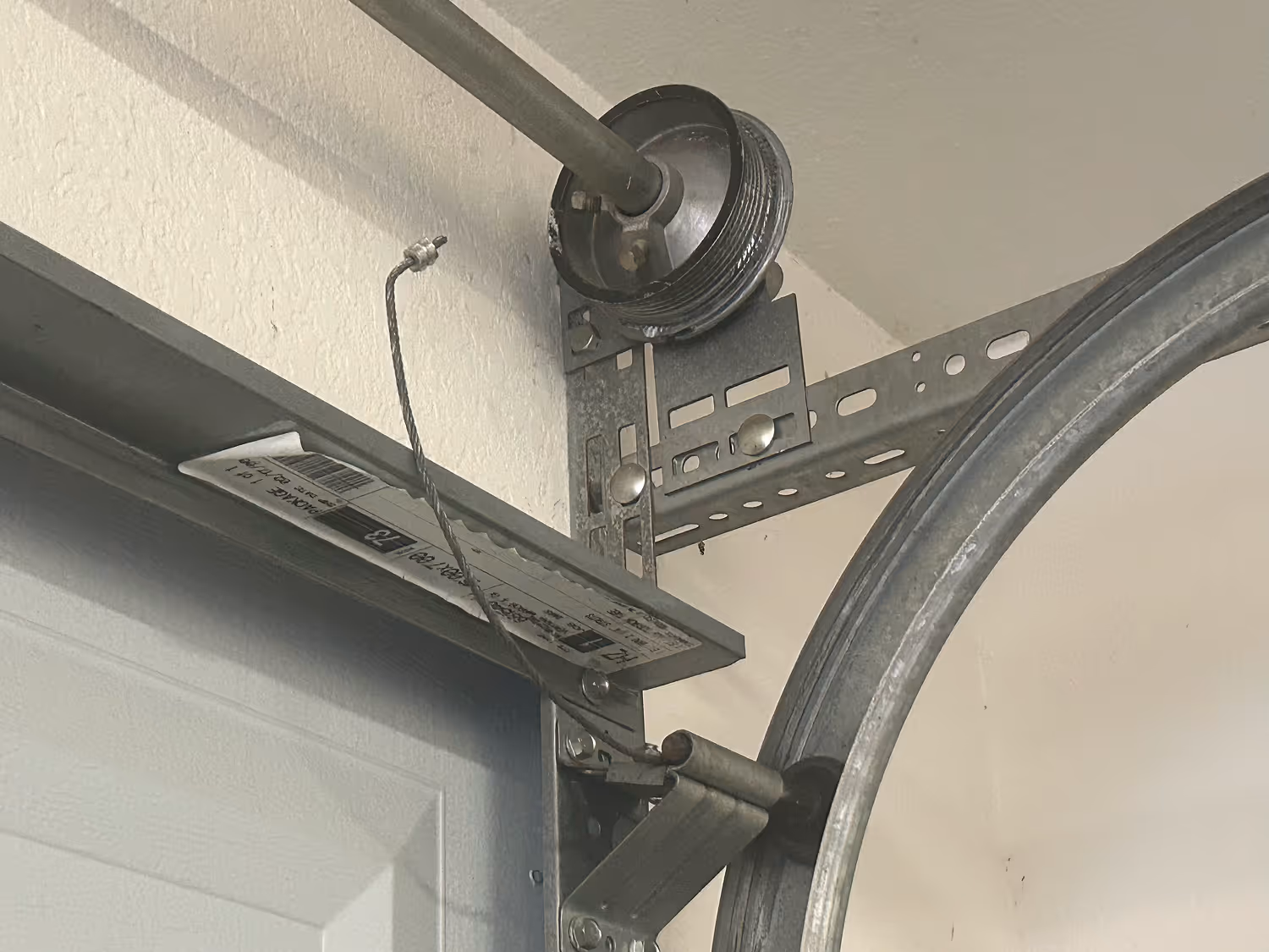 Close-up of a garage door torsion spring assembly with metal pulley and cable attached to a sectional garage door.