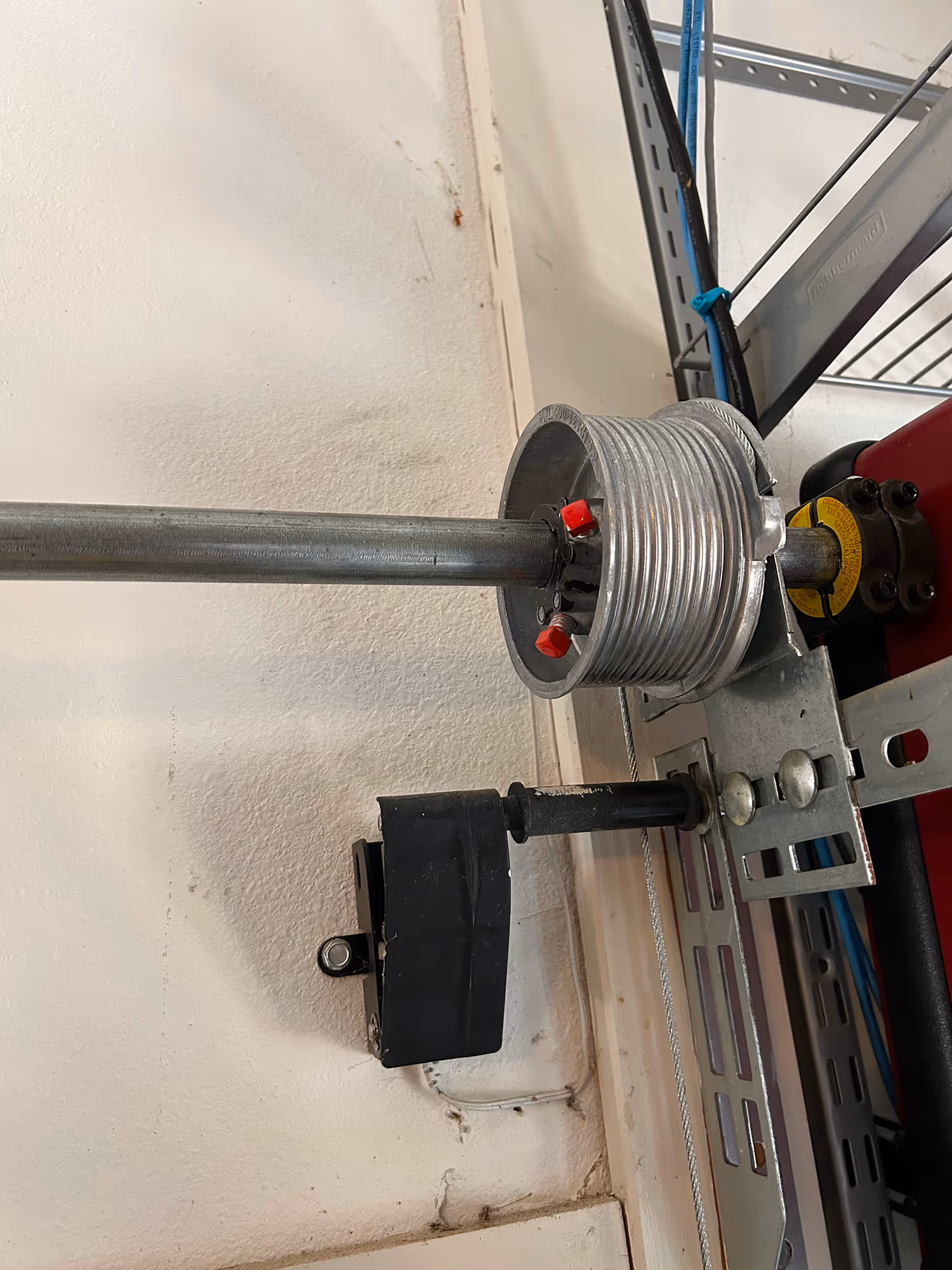 Close-up of a garage door torsion spring system mounted on a wall with metal brackets and a metal rod.