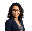 Smiling woman with curly hair wearing glasses and a navy blazer.
