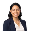 Smiling woman with dark hair wearing a navy blazer and white top against a transparent background.