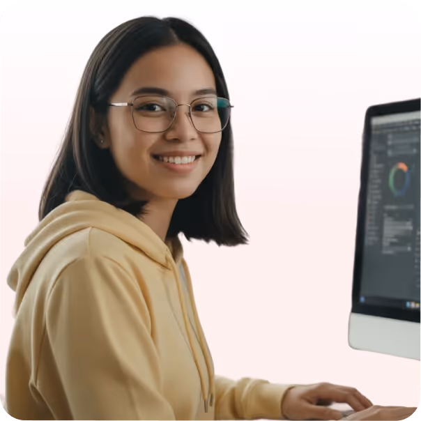 Young woman wearing glasses and a yellow hoodie smiling while working on a computer.