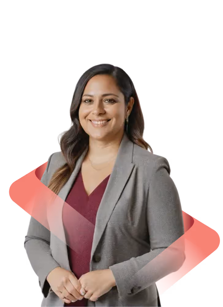 Smiling woman with long dark hair wearing a gray blazer over a maroon top, standing with hands clasped.