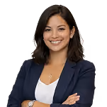 Smiling woman with shoulder-length dark hair wearing a navy blazer over a white top, standing with arms crossed.