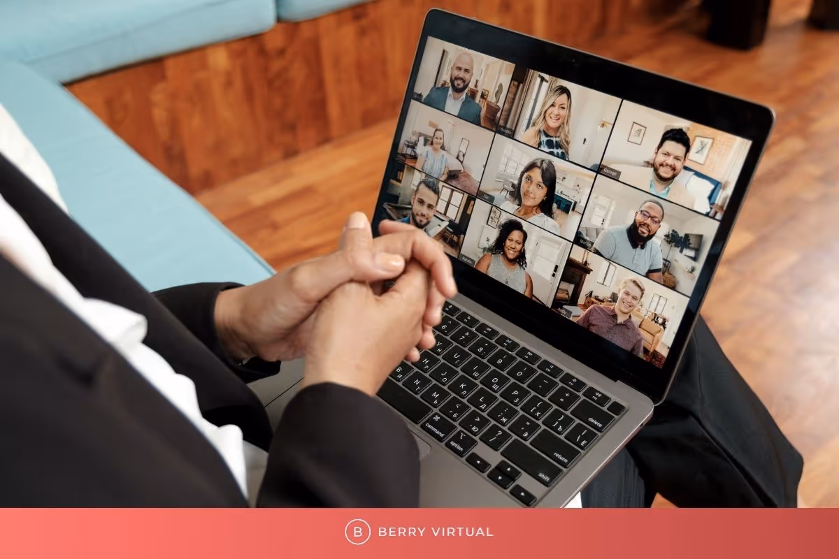 Person on a virtual video call with multiple colleagues displayed in a grid on a laptop screen, seated in a modern workspace. Branding reads 'Berry Virtual'.