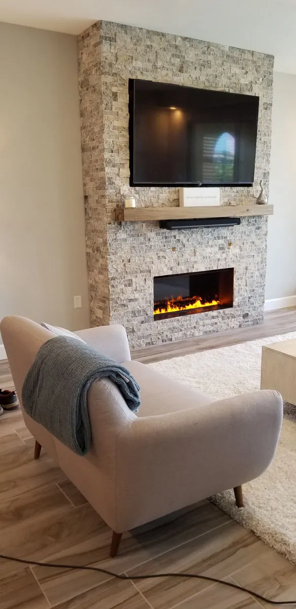 Custom stone accent fireplace wall with wall-mounted TV, floating wood mantel, and electric fireplace insert built by Florida building contractor