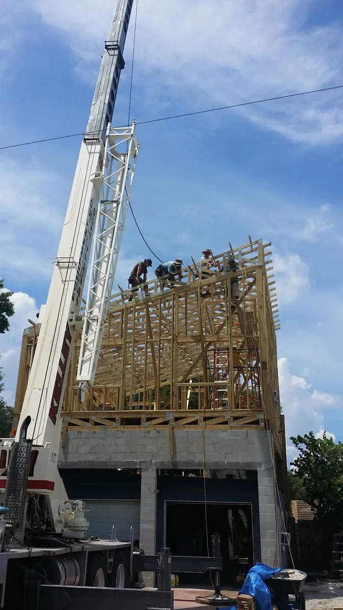 Florida building contractor crew using a crane to install wooden roof trusses on a new two-story concrete block home construction project