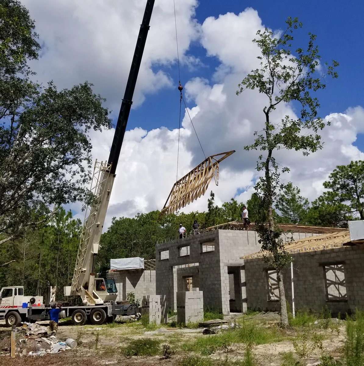 Crane lifting a prefabricated roof truss into place on a Florida building contractor new home construction site