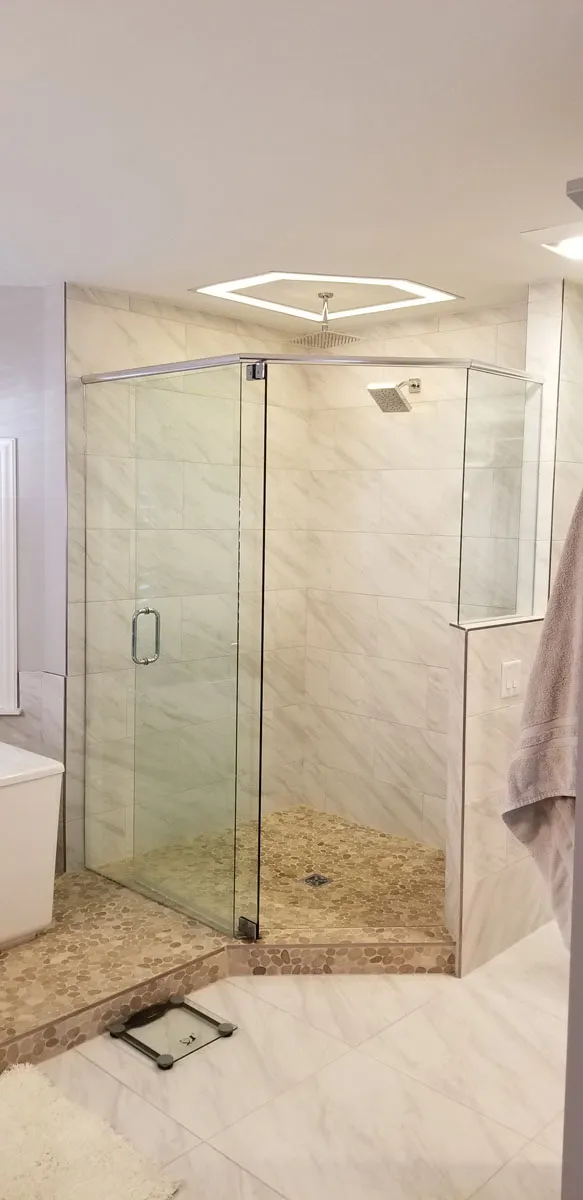 Corner glass-enclosed shower with marble wall tile, pebble stone floor, and rain shower head installed by Florida building contractor