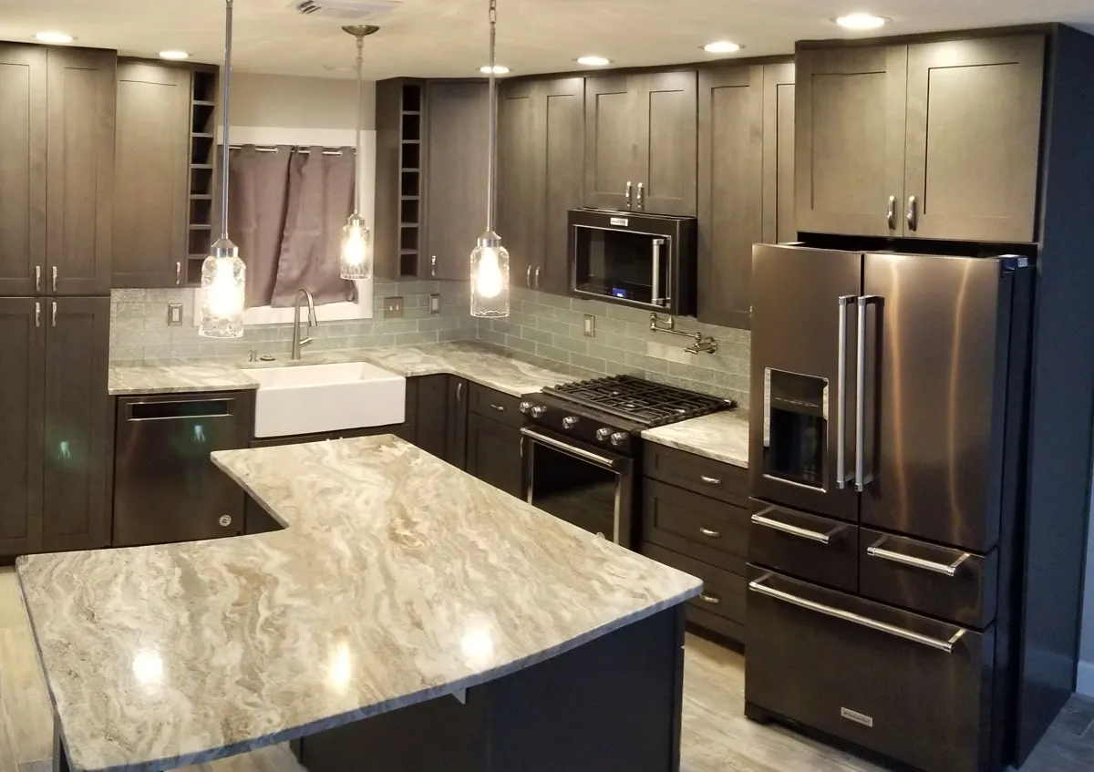 Kitchen remodel by Florida building contractor with dark shaker cabinets, swirl granite countertop island, farmhouse sink, and pendant lighting