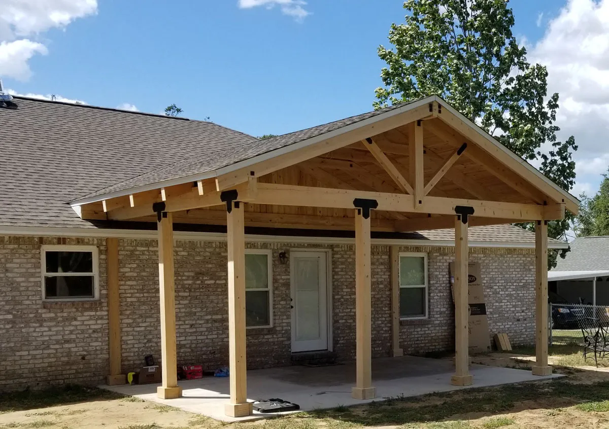 Custom covered patio addition by Florida building contractor with exposed timber beam frame and steel bracket hardware on a brick home