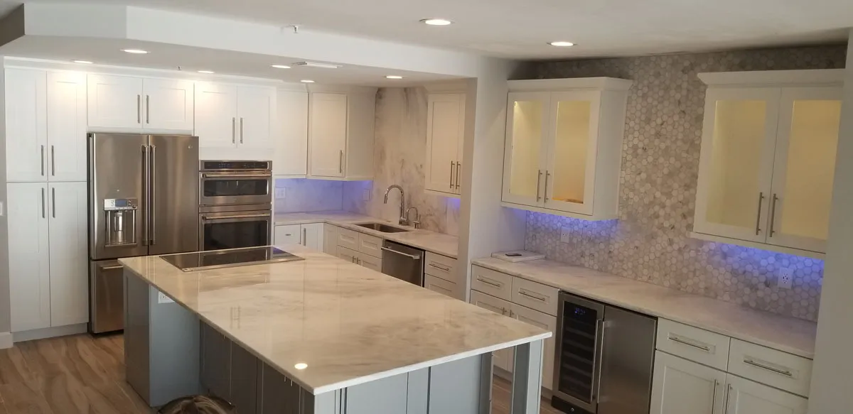 Modern kitchen remodel by Florida building contractor with marble countertops, white shaker cabinets, stainless steel appliances, and LED under-cabinet lighting