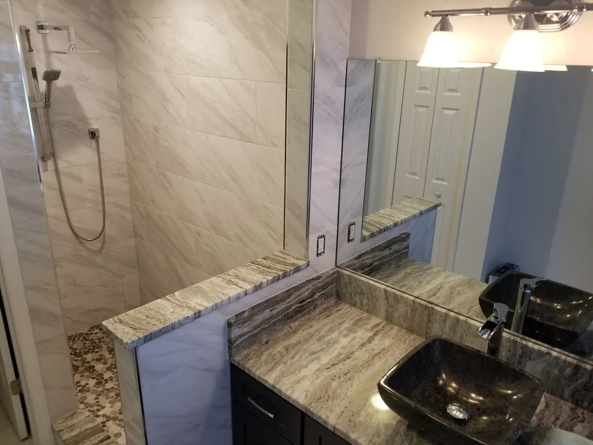 Bathroom renovation by Florida building contractor with granite vessel sink, marble tiled walk-in shower, and pebble stone floor