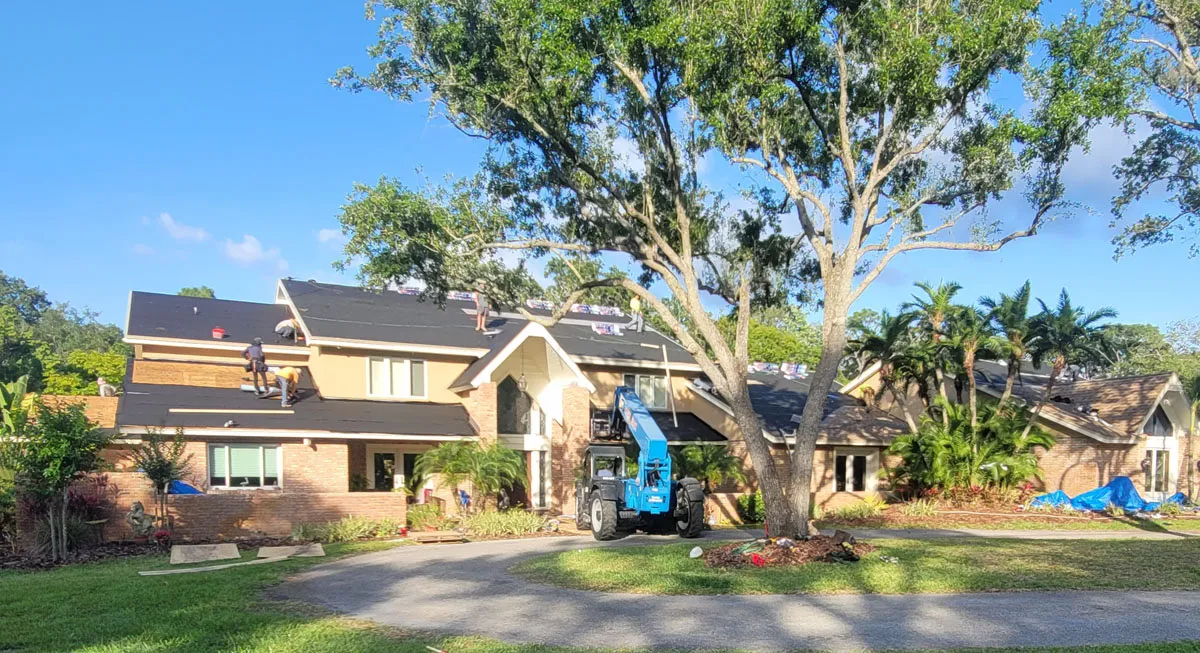 Florida building contractor performing a full roof replacement on a two-story brick and stucco home using a boom lift