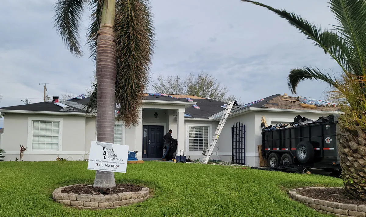 Florida building contractor roof replacement project on a ranch-style home with company yard sign, palm trees, and dumpster trailer on site