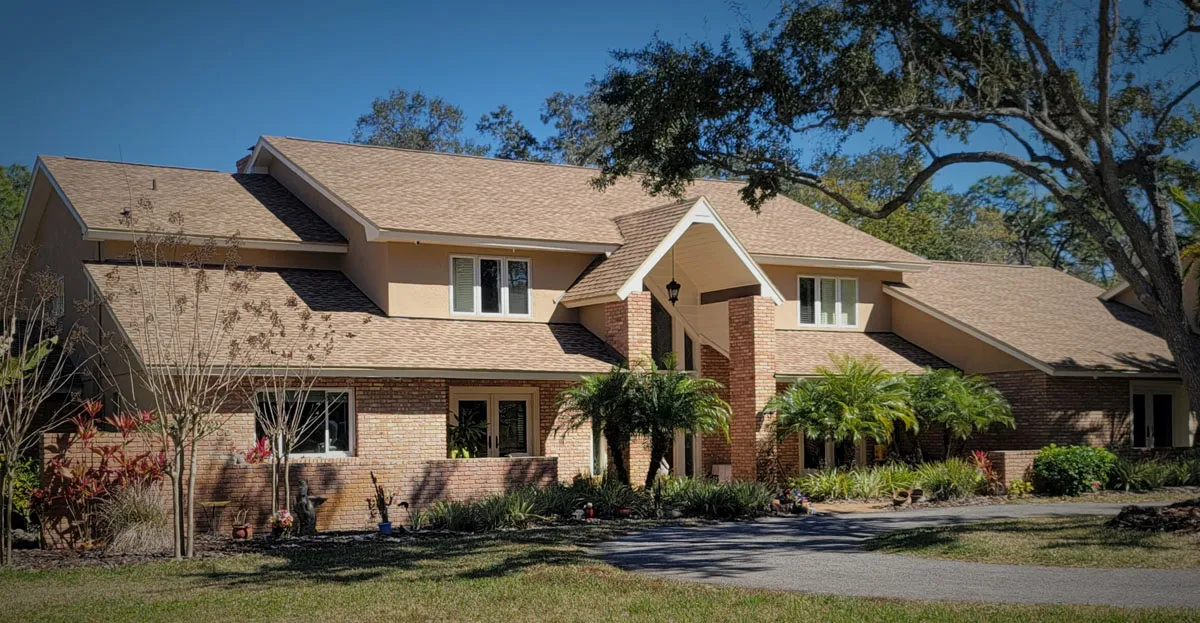 Completed two-story brick and stucco home with new shingle roof, tropical landscaping, and covered entryway by Florida building contractor
