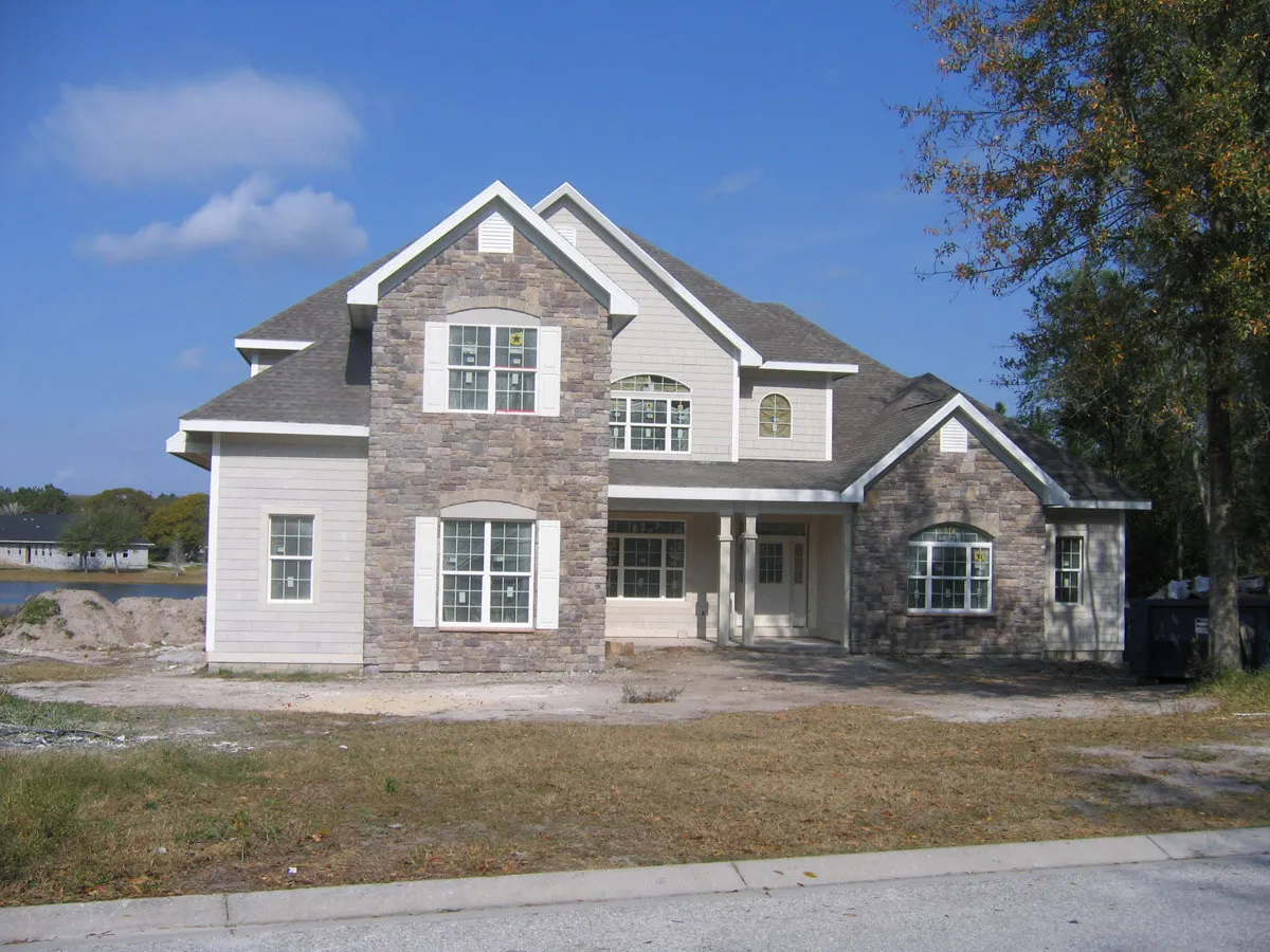 New construction two-story home by Florida building contractor with stone and siding exterior, arched windows, and covered front porch