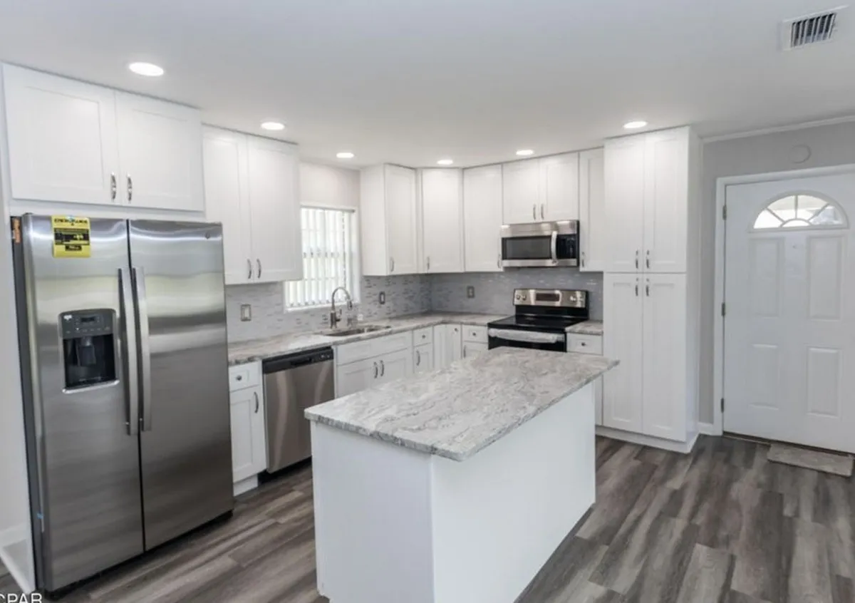 White cabinet kitchen remodel by Florida building contractor with granite island countertop, stainless steel appliances, and glass tile backsplash