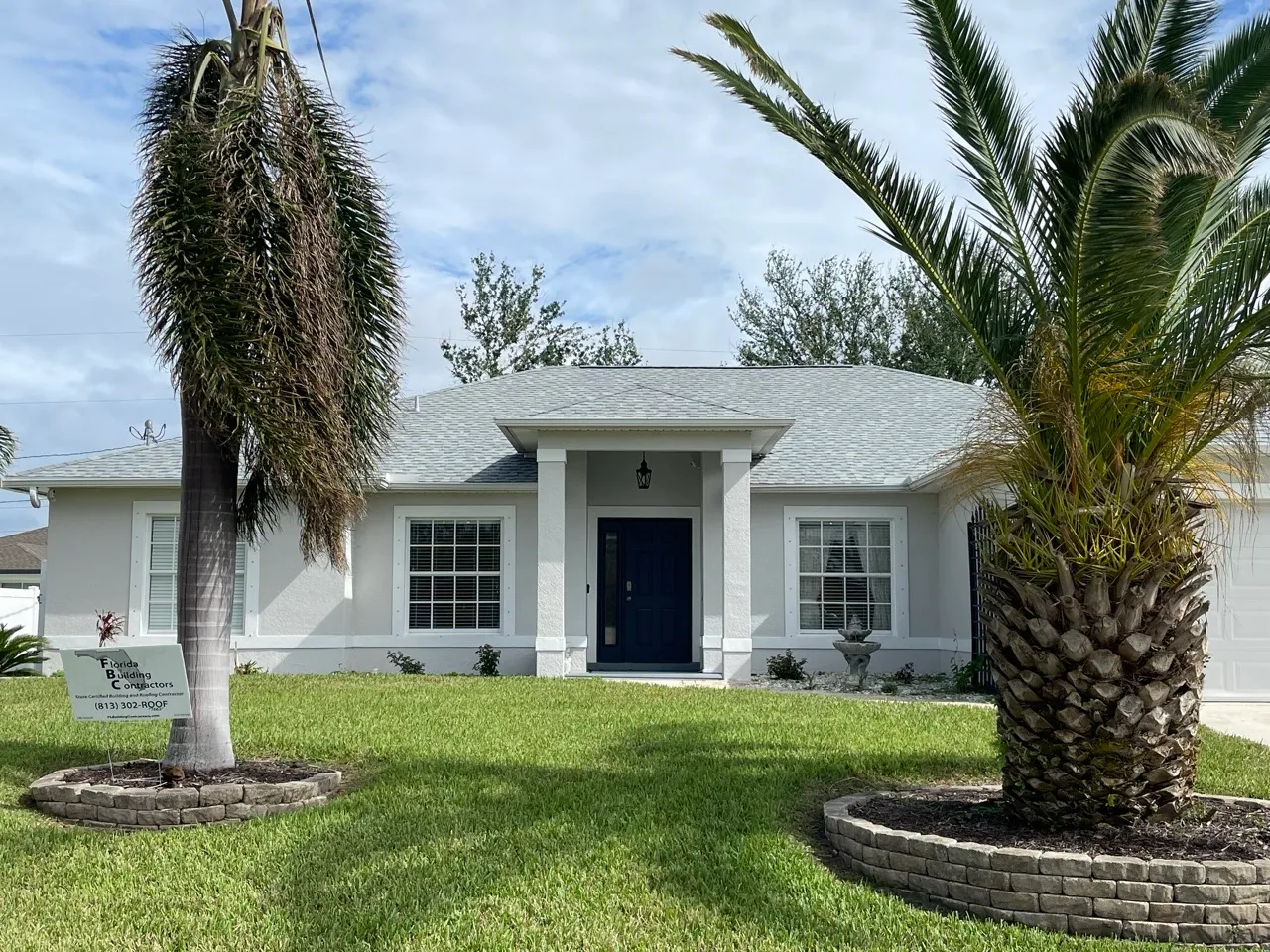 White single-story house with gray roof, two palm trees in the front yard, and a sign for Florida Building Contractors.