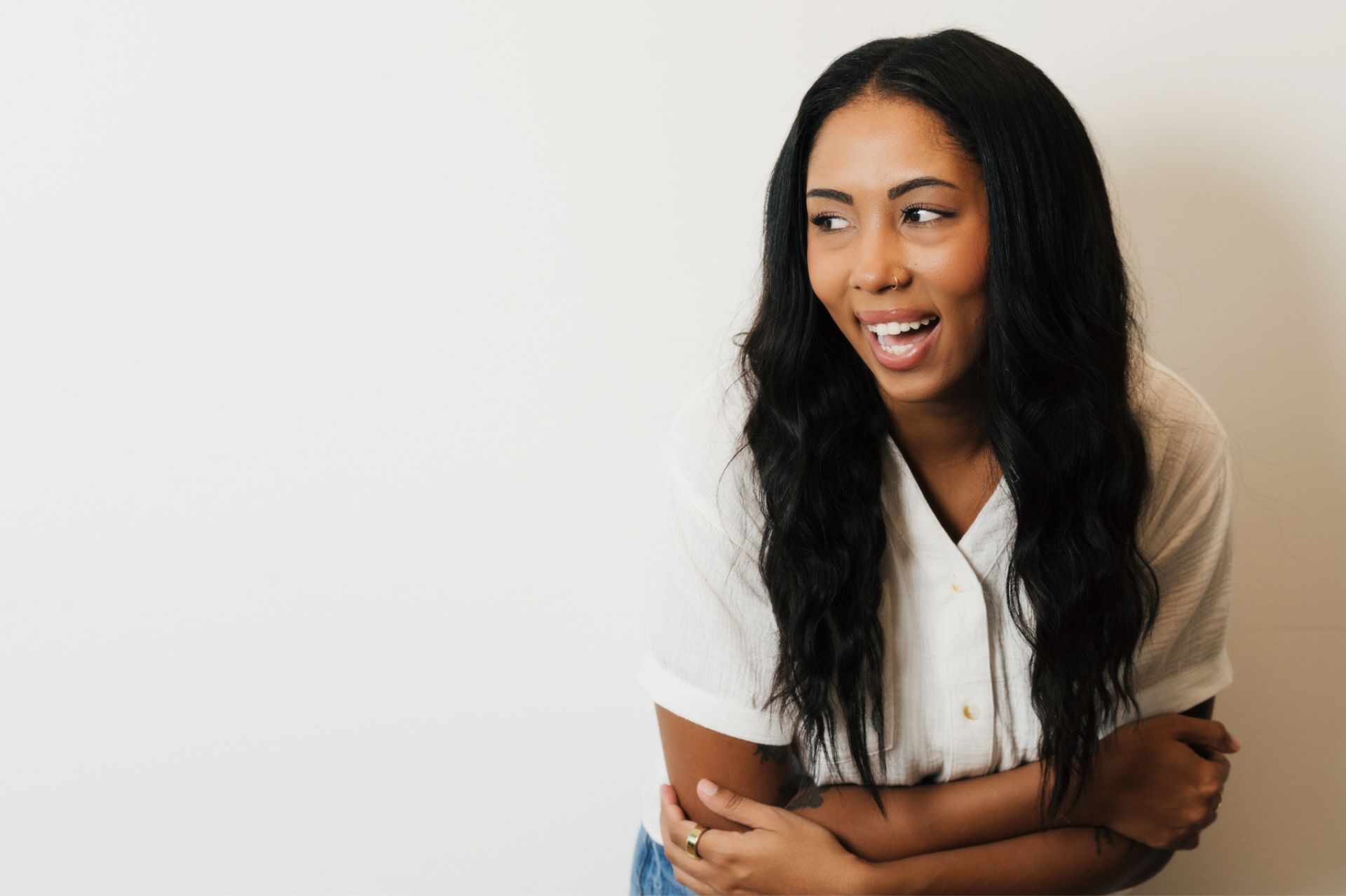 Smiling woman with long black hair and a nose ring wearing a white shirt against a white background.
