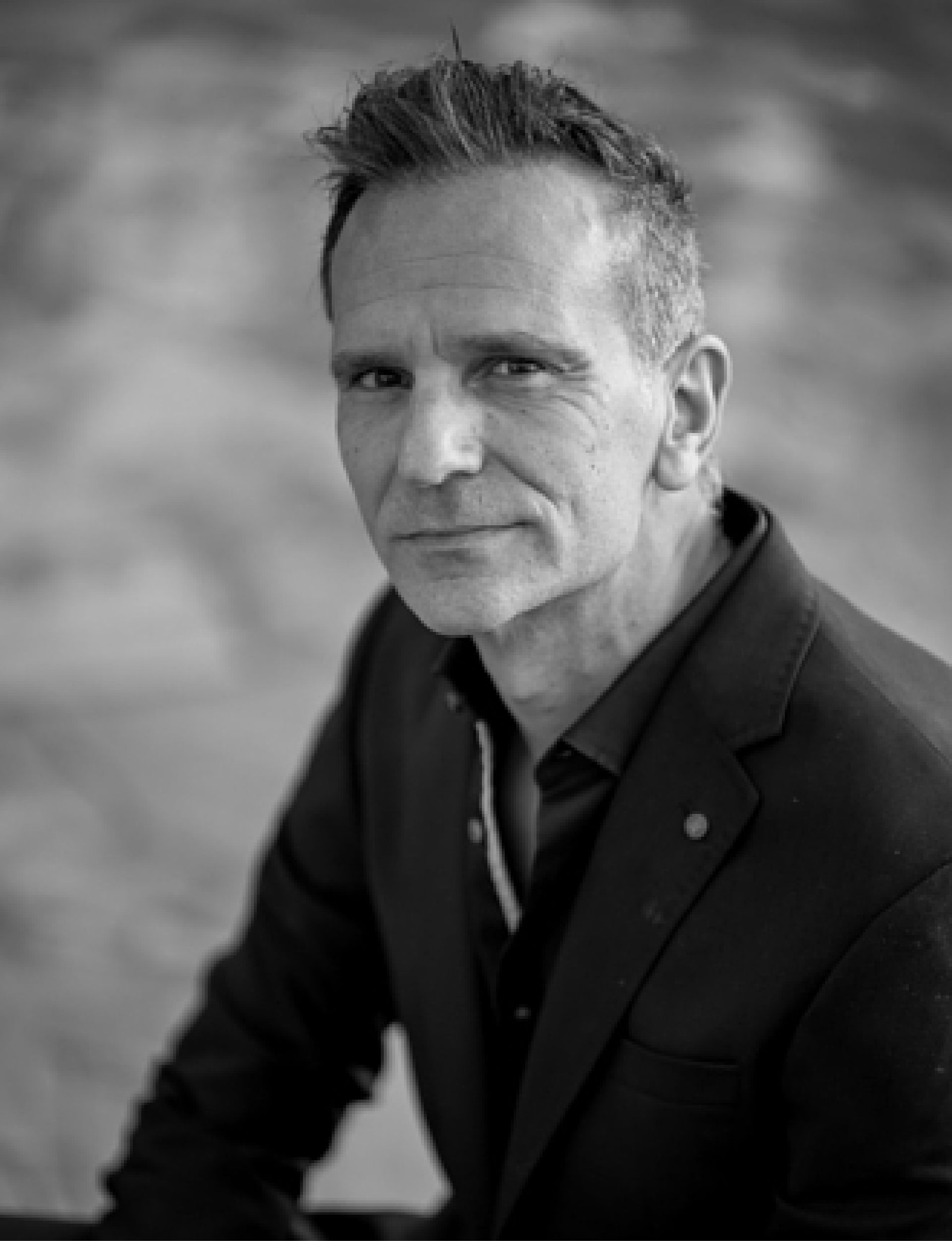 Black and white portrait of a middle-aged man in a blazer looking at the camera with a slight smile.