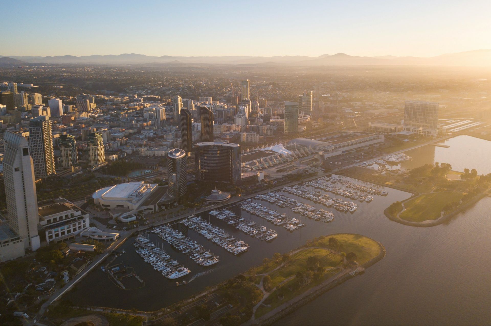 Aerial view of a coastal city skyline with a marina filled with boats at sunset.
