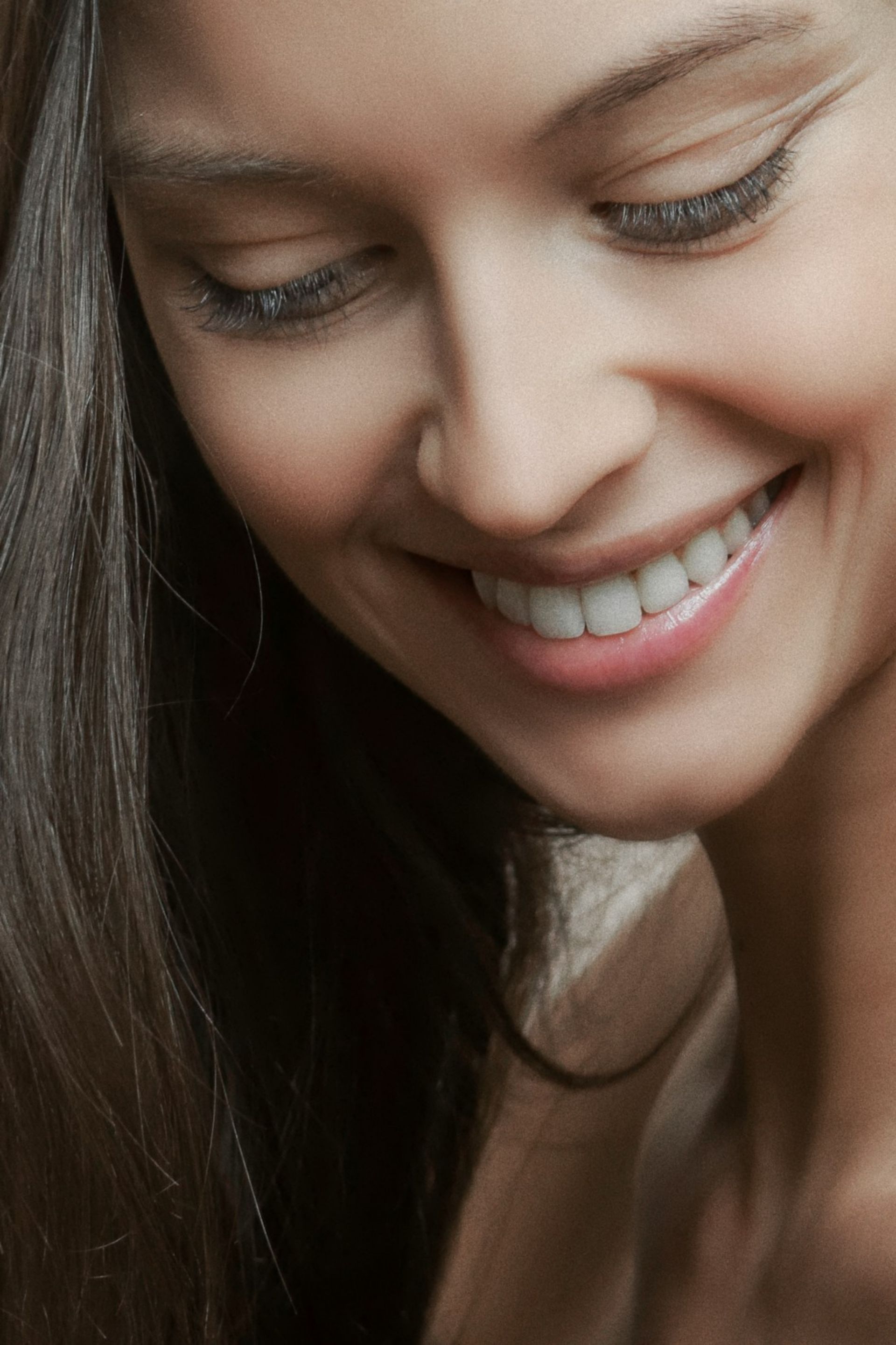 Close-up of a woman smiling with long dark hair and closed eyes.