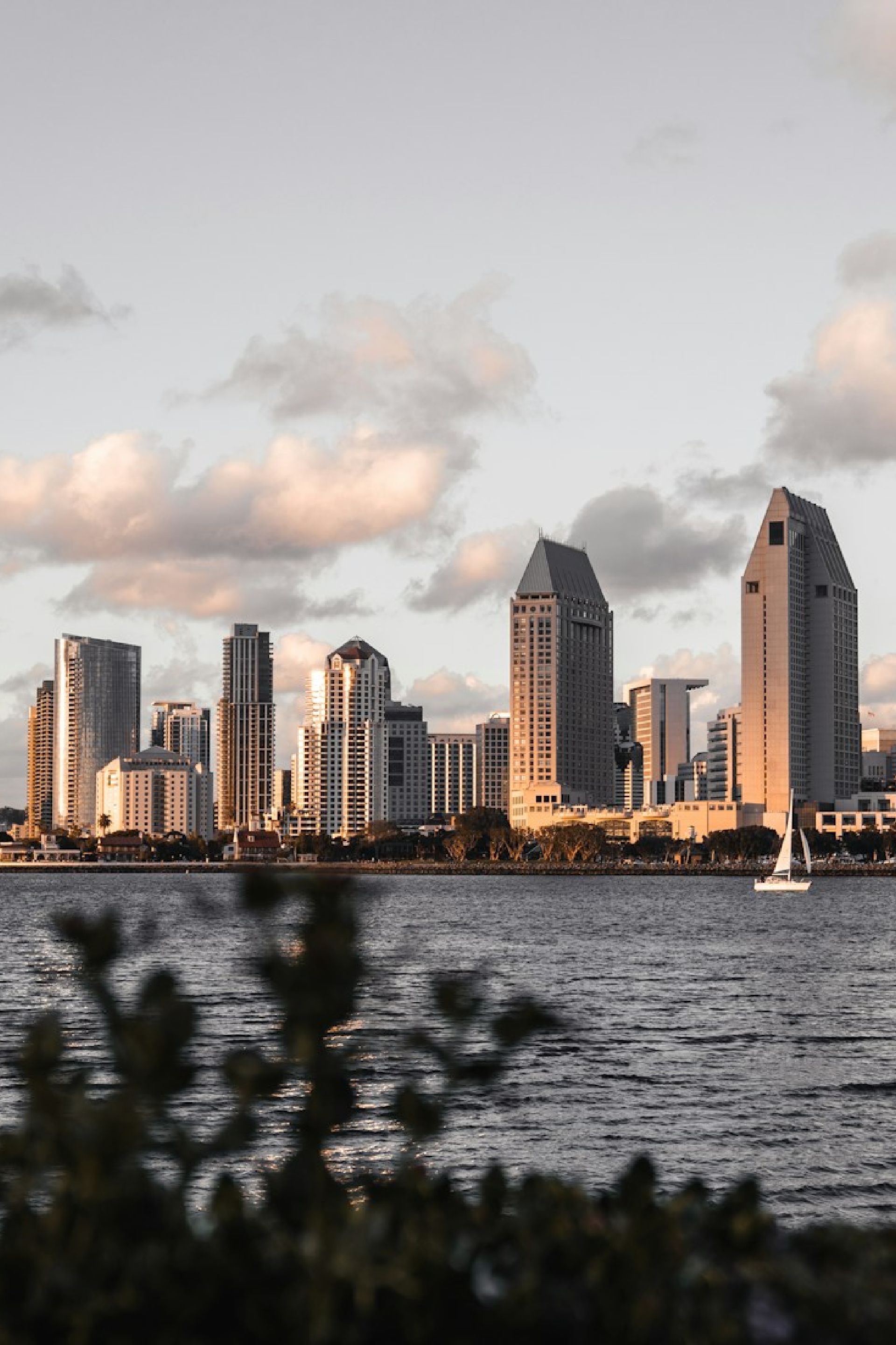 San Diego city skyline at sunset with water in foreground and a sailboat on the right.