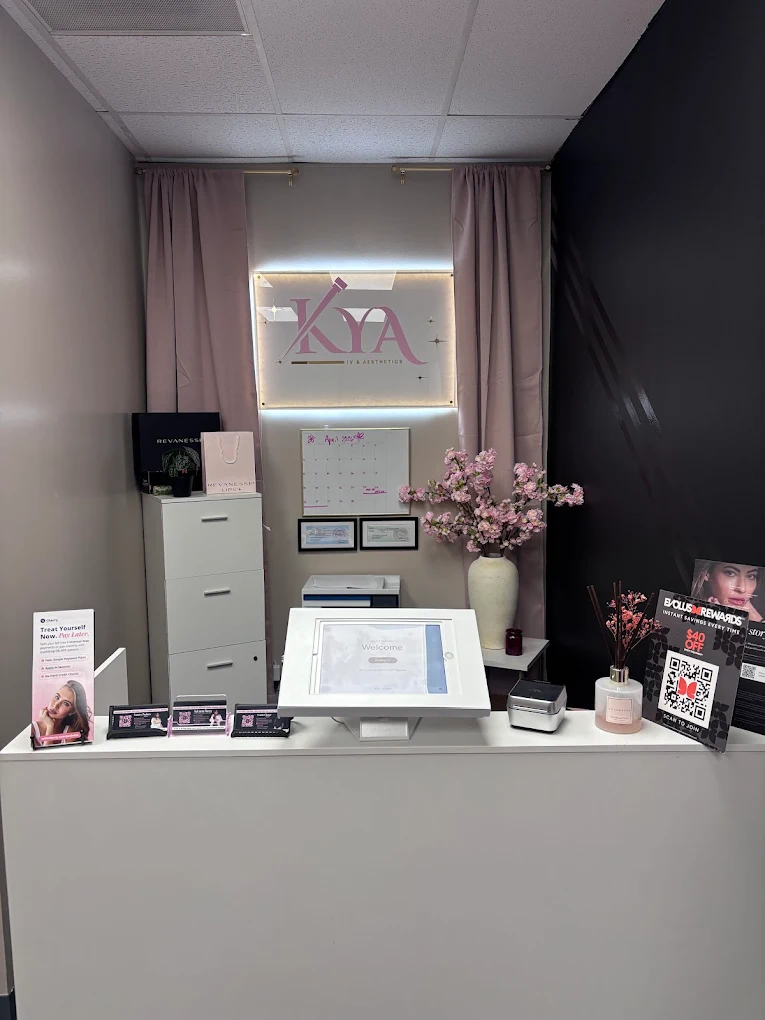 Reception desk at KYA Ink & Aesthetics with tablet, flower vase, calendar, and promotional signs.
