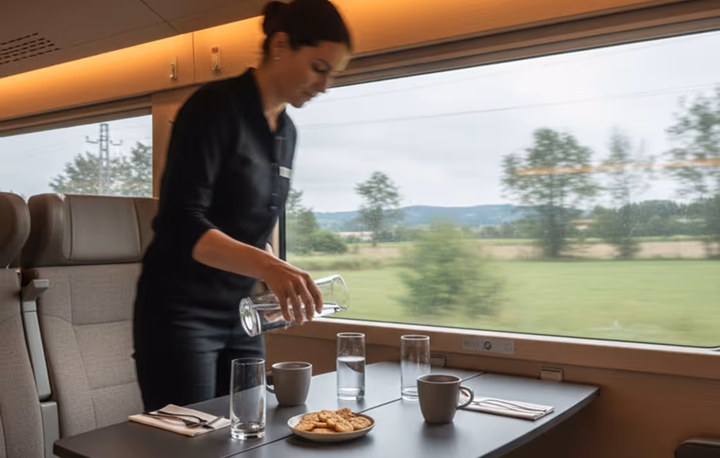Onboard service: Staff member preparing service inside a premium train cabin.