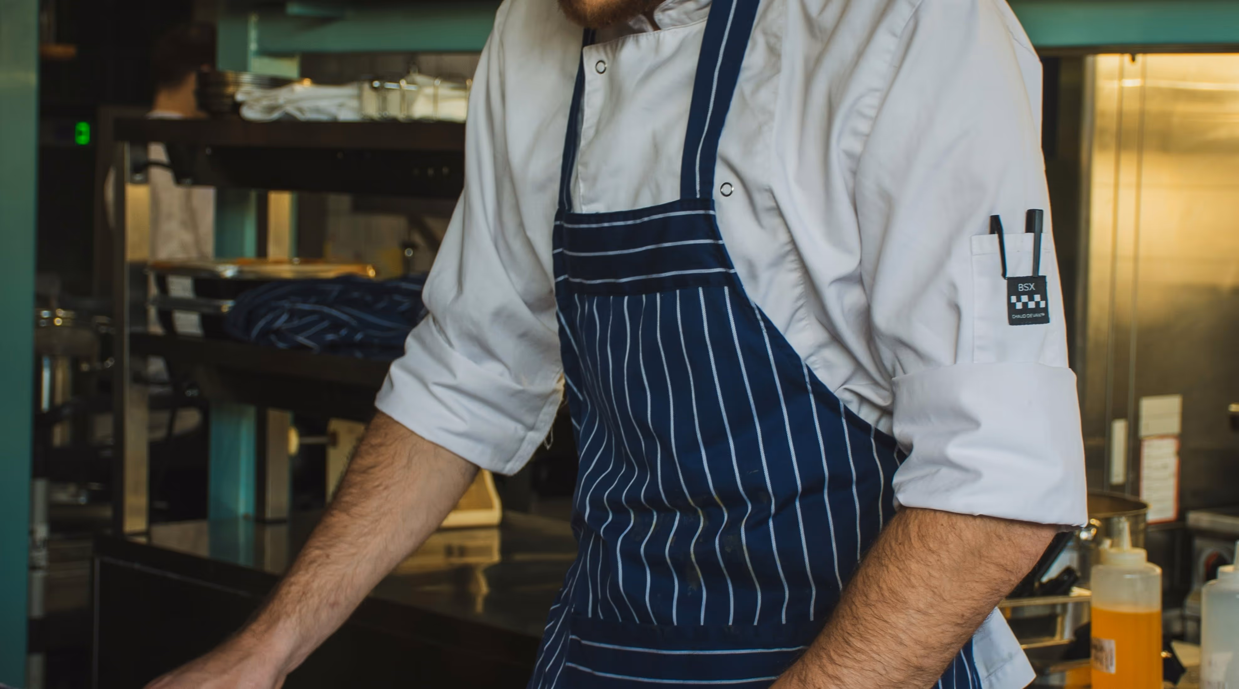 Chef wearing a white uniform and blue pinstriped apron working in a kitchen.