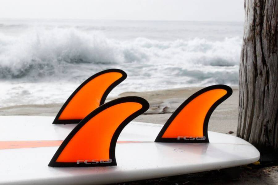 Three orange fins fitted to a surfboard on the beach