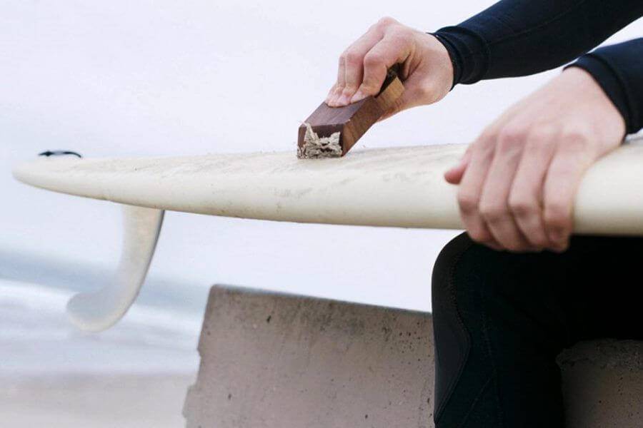 Hands applying wax to a surfboard deck