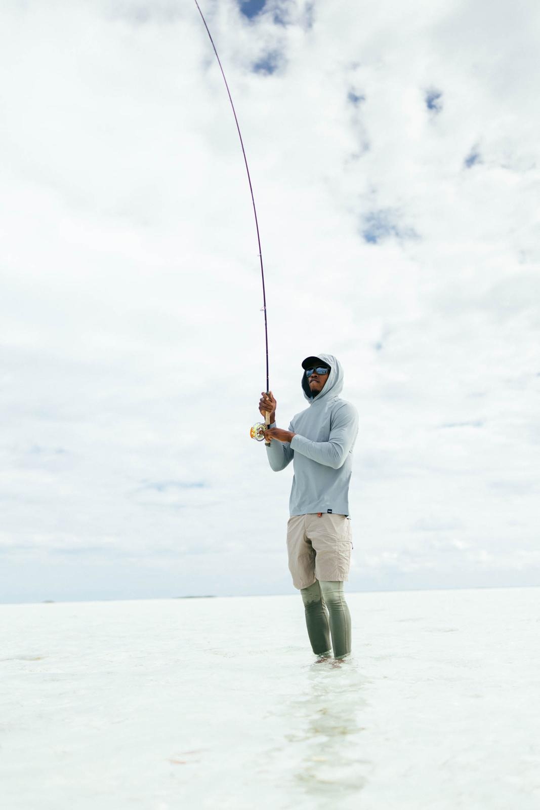LJ Bean wading a white sand flat with his fly rod bent on a fish