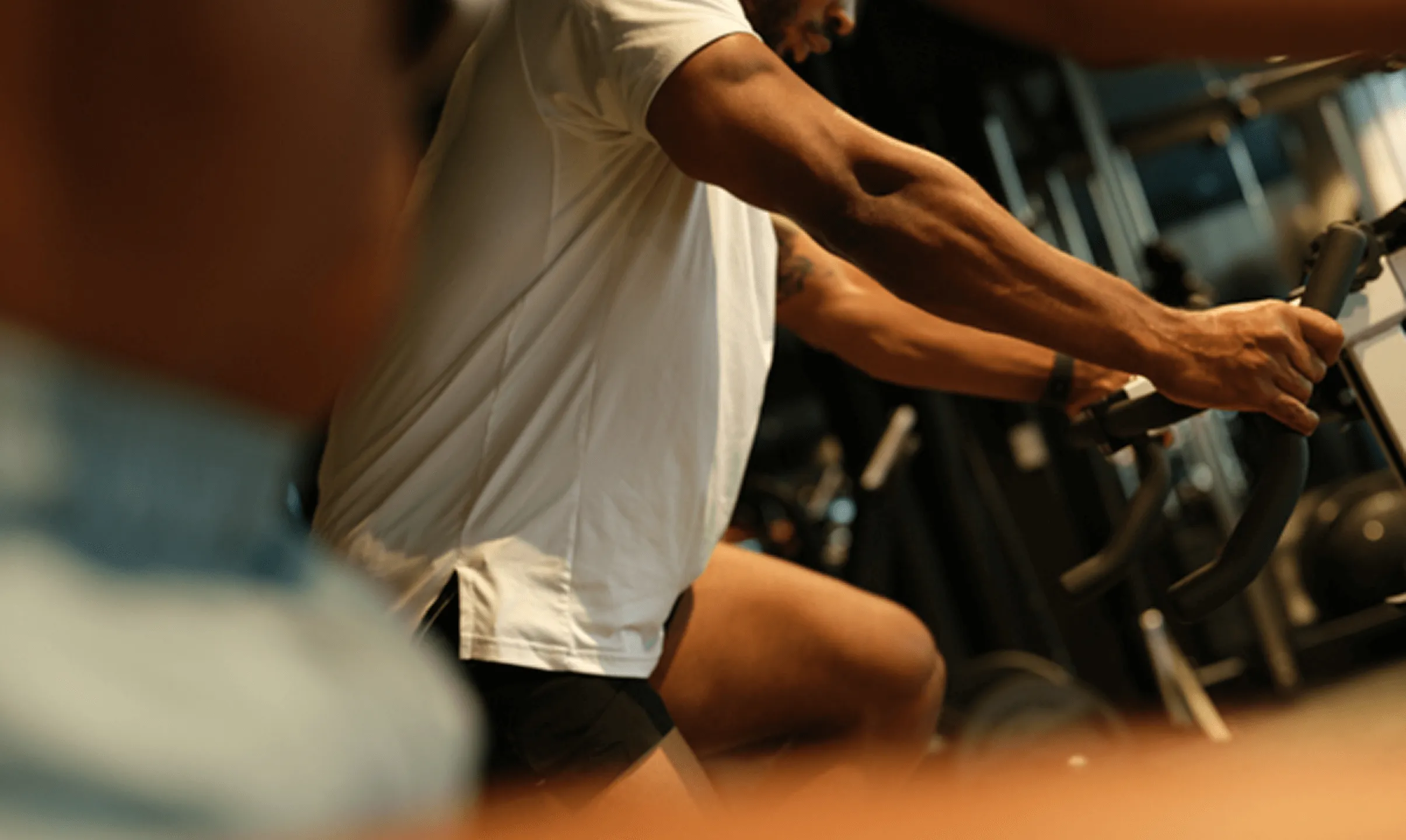 Person wearing a white shirt exercising on a stationary bike in a gym.