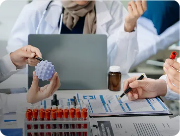 Medical professionals in lab coats examining a virus model and reviewing charts with test tubes on the table.