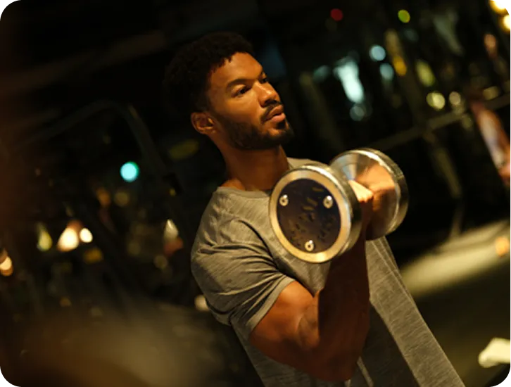 Man wearing gray shirt lifting a dumbbell in a dimly lit gym.