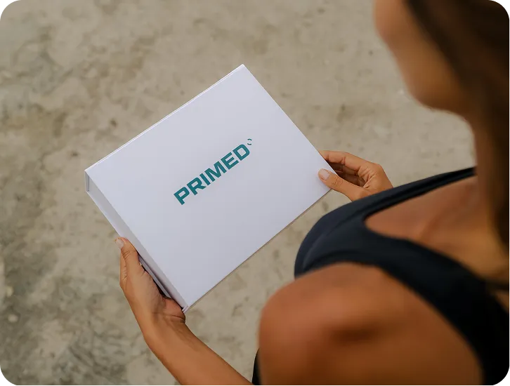 Woman holding a white box with the word PRIMED printed in teal letters.