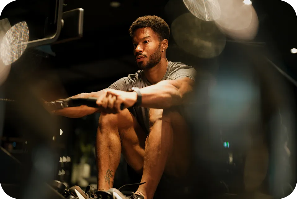 Focused man using a rowing machine for exercise in a dimly lit gym.