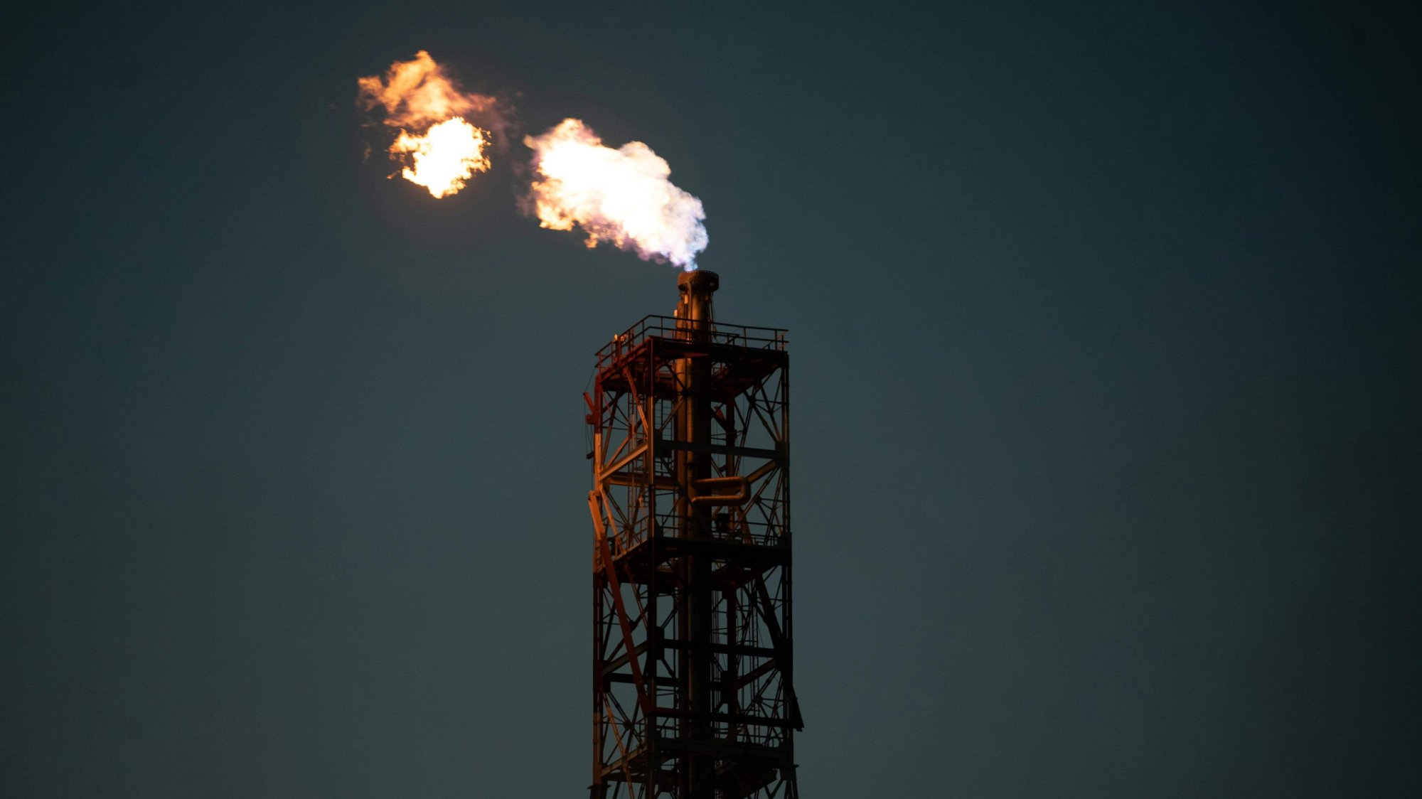 Industrial flare stack burning off gas against a dark night sky.